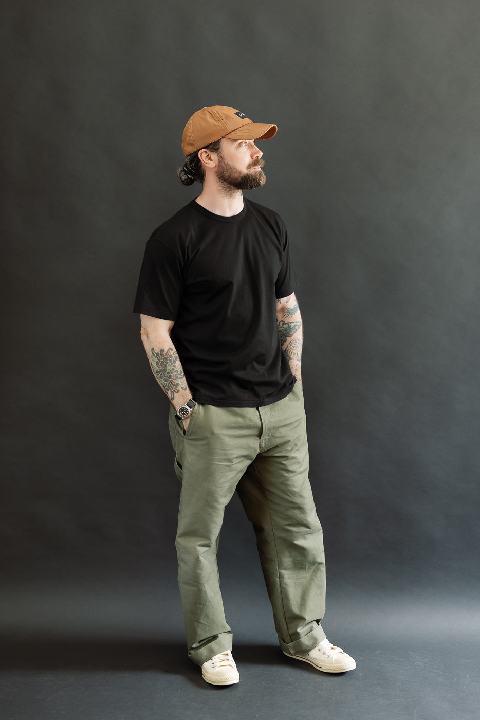 Full-length portrait of a man wearing the Ultimate Pima Tsuriami Crewneck T-Shirt in black, showcasing its relaxed fit and smooth texture, styled with olive-green pants and off-white sneakers.