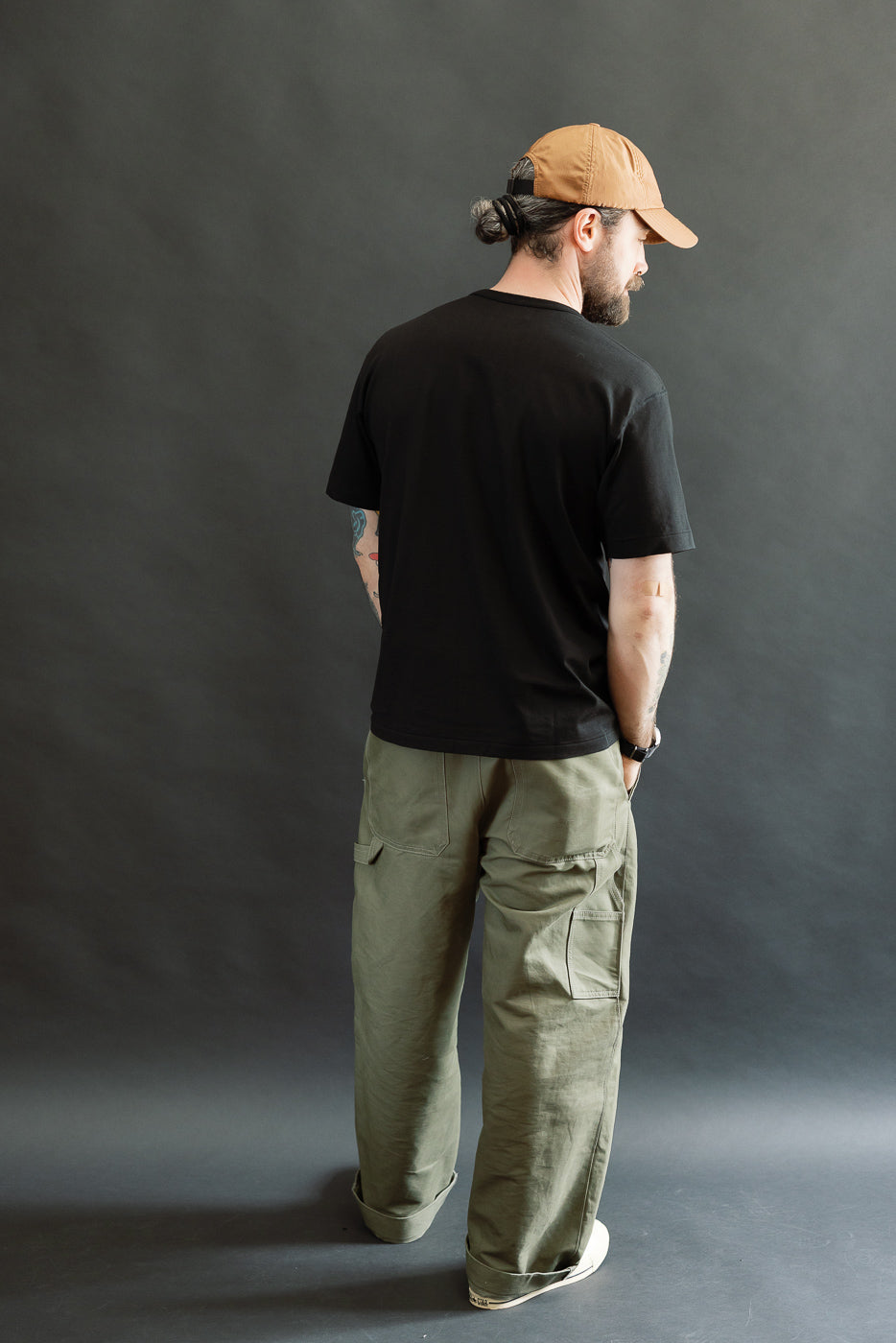A man wearing the Ultimate Pima Tsuriami Crewneck T-Shirt in black, styled with olive cargo pants and off-white sneakers, showcases the shirt's athletic fit and premium craftsmanship.