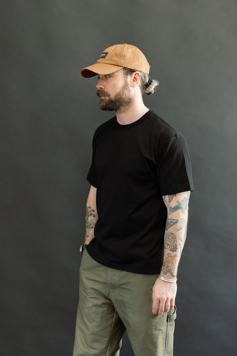Man in profile wearing Ultimate Pima Tsuriami Crewneck T-Shirt - Black, showcasing its smooth, lightweight fabric and athletic fit. His forearms display colorful tattoos, adding a stylish, personal touch.