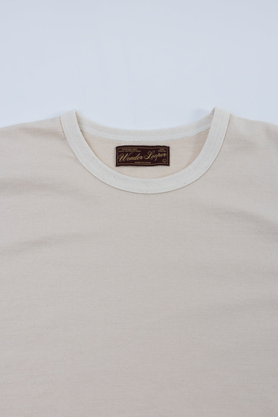 The Ultimate Pima Tsuriami Crewneck T-Shirt - Ecru features a light-beige shade and a woven Wonder Looper label below the crew-neck, showcasing its Japanese craftsmanship and premium fabric.