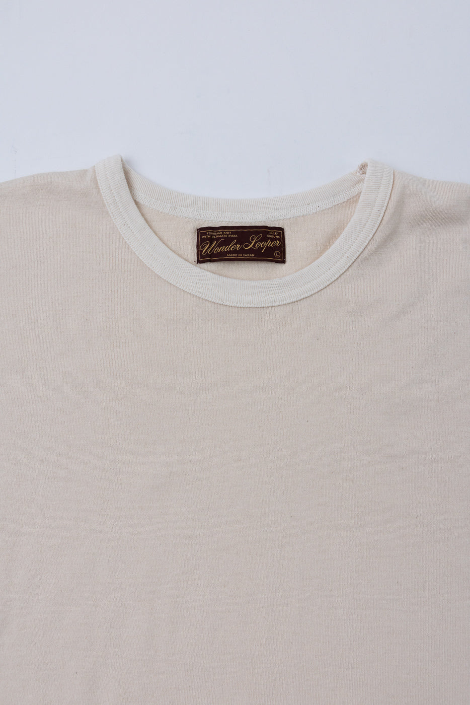 Close-up front view of the crew neck collar and Wonder Looper brand tag on a cream t-shirt.