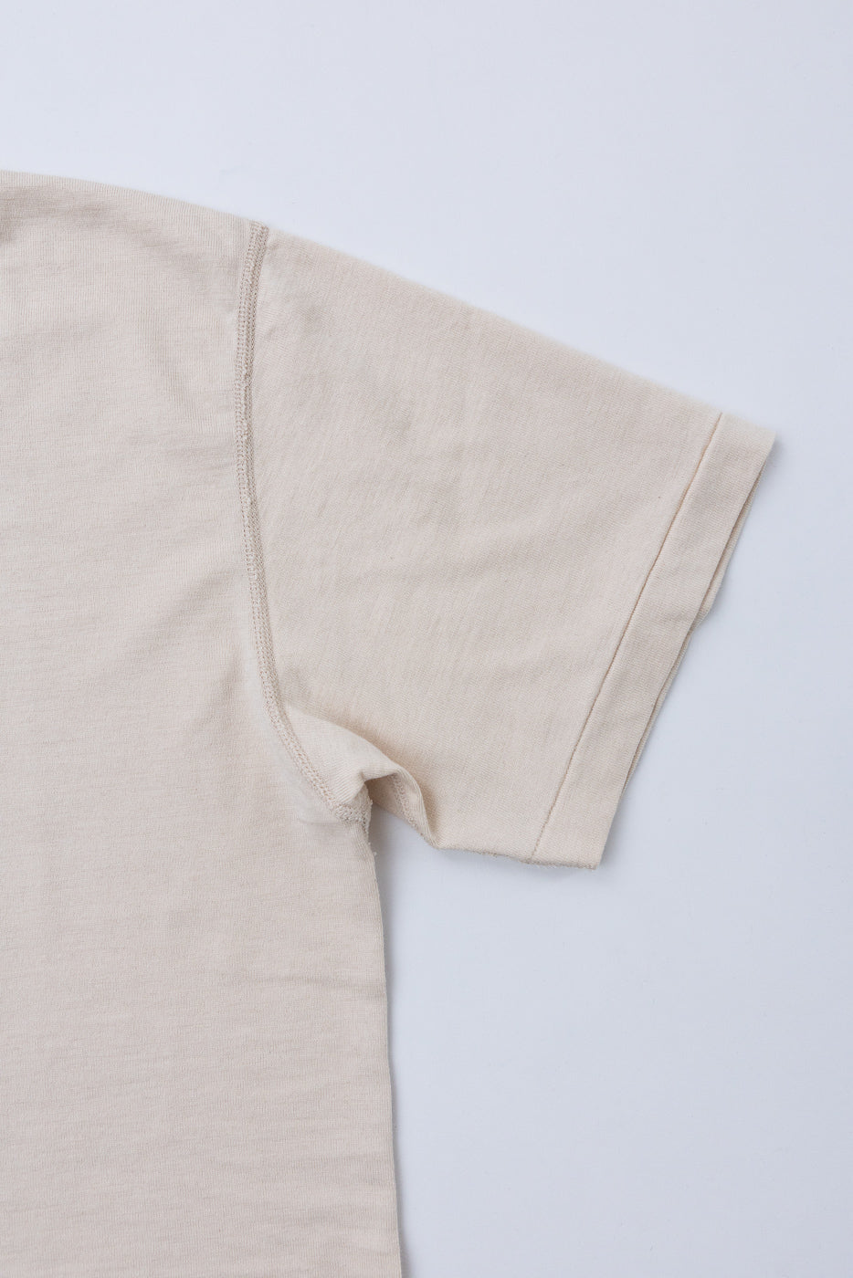 Close-up of the front right sleeve and shoulder of a beige short-sleeve t-shirt.