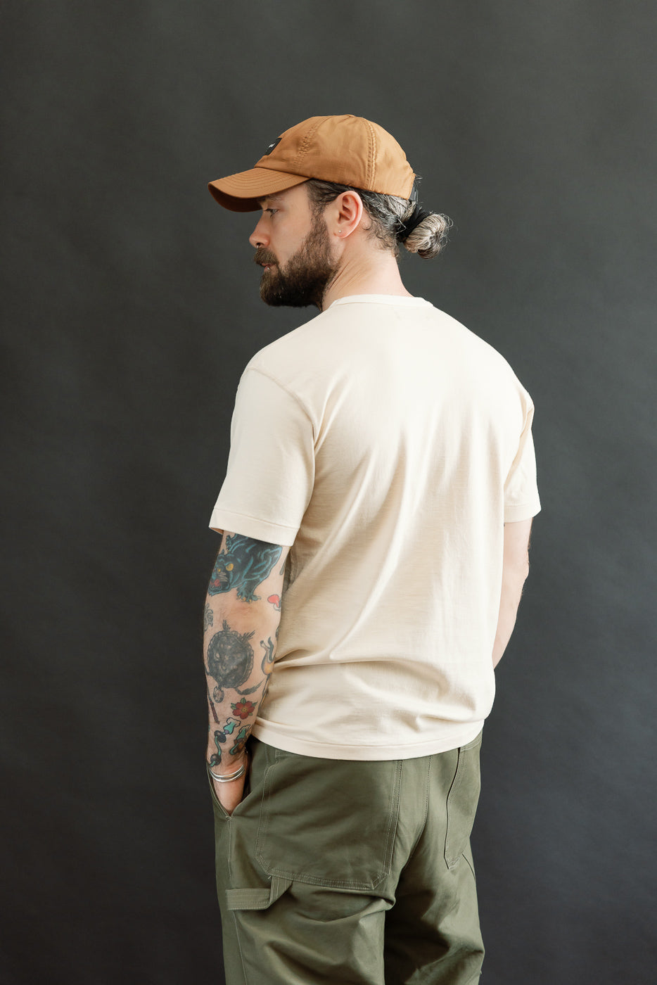 Man in light-beige Ultimate Pima Tsuriami Crewneck T-Shirt, showcasing its smooth texture and athletic fit, paired with olive-green cargo pants and a brown cap, highlighting Dant's premium Japanese-American apparel.