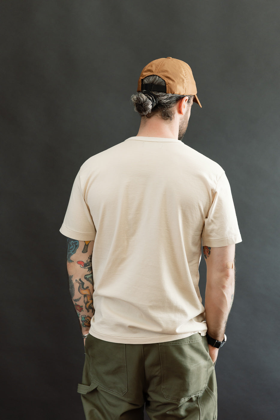 Man wearing the Ultimate Pima Tsuriami Crewneck T-Shirt - Ecru, showcasing its smooth, lightweight fabric and athletic fit, complemented by olive-green cargo pants and a tan baseball cap.