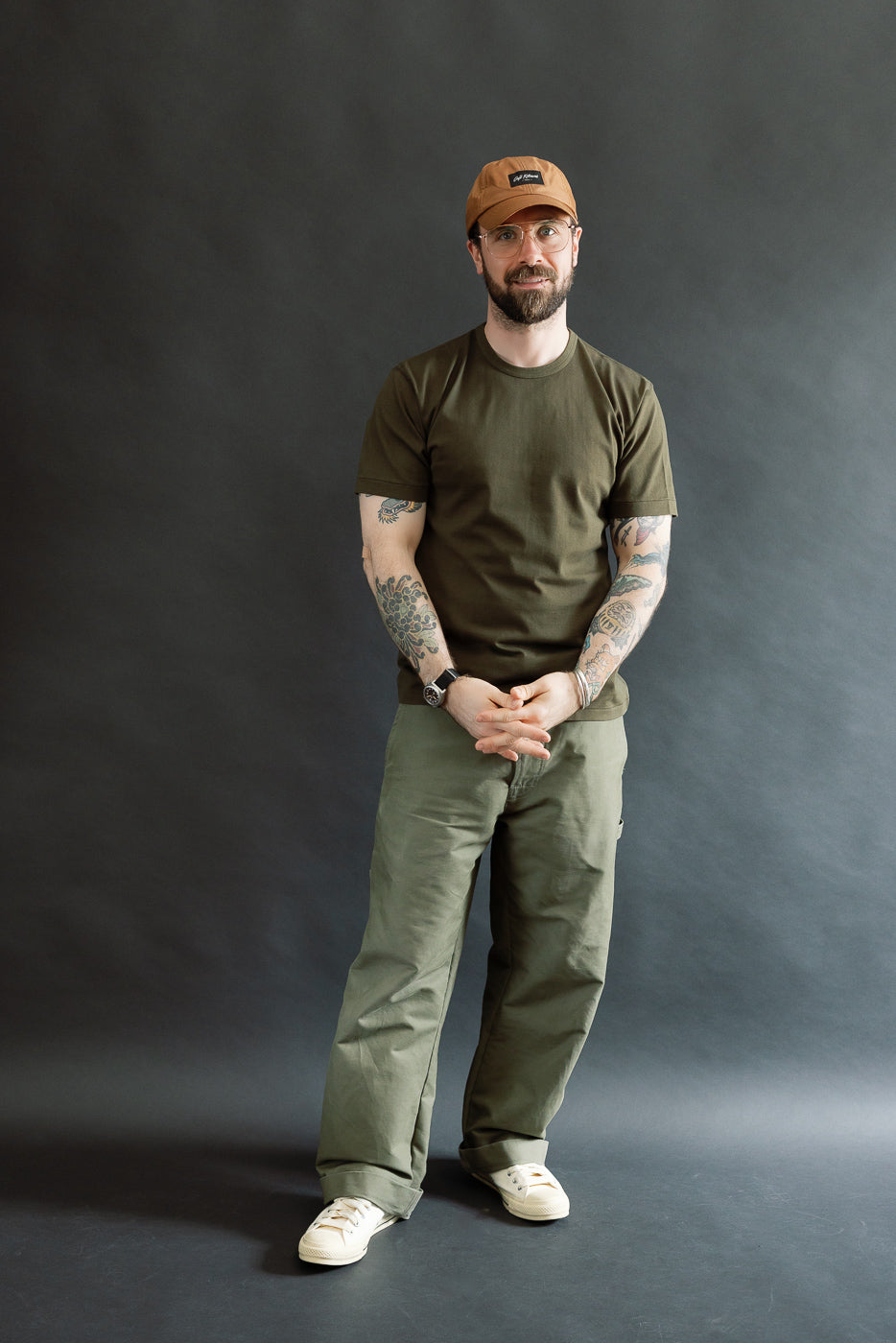Man wearing Ultimate Pima Tsuriami Crewneck T-Shirt - Khaki stands confidently, showcasing the t-shirt's smooth texture and relaxed fit, paired with loose olive pants and off-white sneakers.