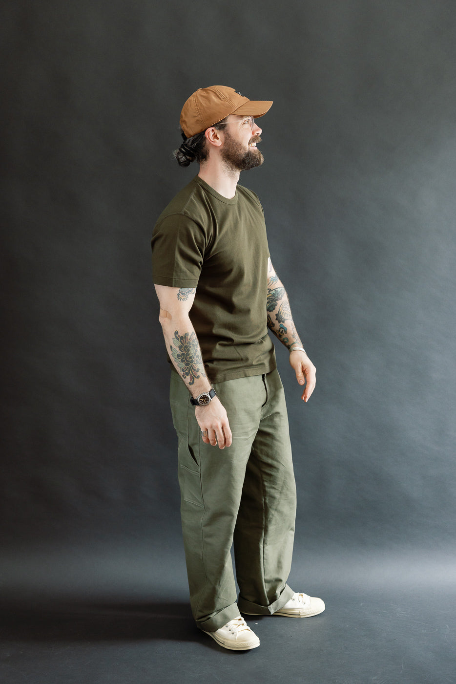 Man in profile wearing the Ultimate Pima Tsuriami Crewneck T-Shirt - Khaki, showcasing its casual, utilitarian style with olive-green pants and off-white sneakers, embodying Dant's premium, heritage-inspired menswear ethos.