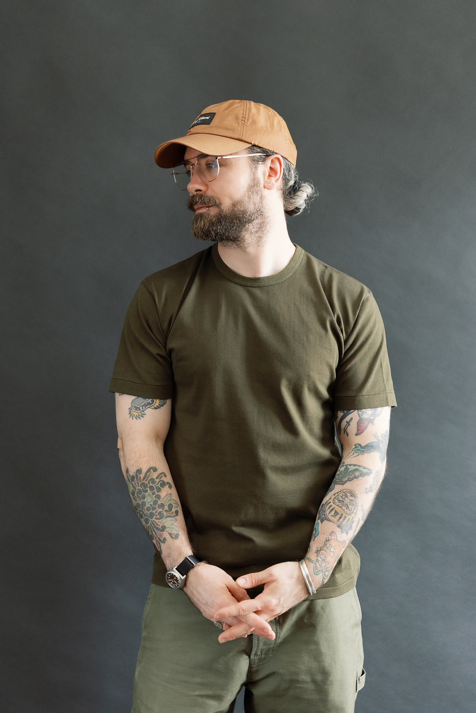 A man models the Ultimate Pima Tsuriami Crewneck T-Shirt - Khaki, showcasing its smooth, lightweight fabric and athletic fit. He pairs it with matching olive-green pants, embodying Dant's premium menswear style.