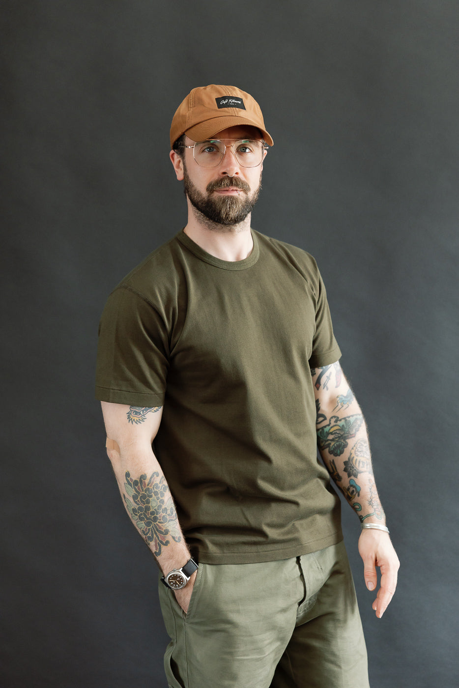 Man wearing the Ultimate Pima Tsuriami Crewneck T-Shirt - Khaki with tattoos on forearms, showcasing its smooth texture and athletic fit. The shirt is made of 100% organic Pima cotton.