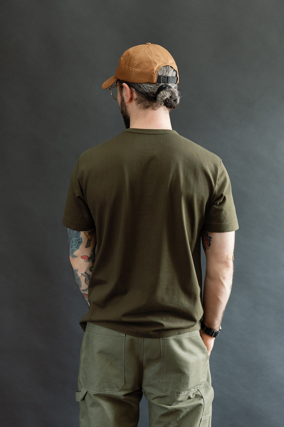 A man models the Ultimate Pima Tsuriami Crewneck T-Shirt in Khaki, showcasing its light, smooth texture and athletic fit. He pairs it with olive cargo pants and a brown cap.