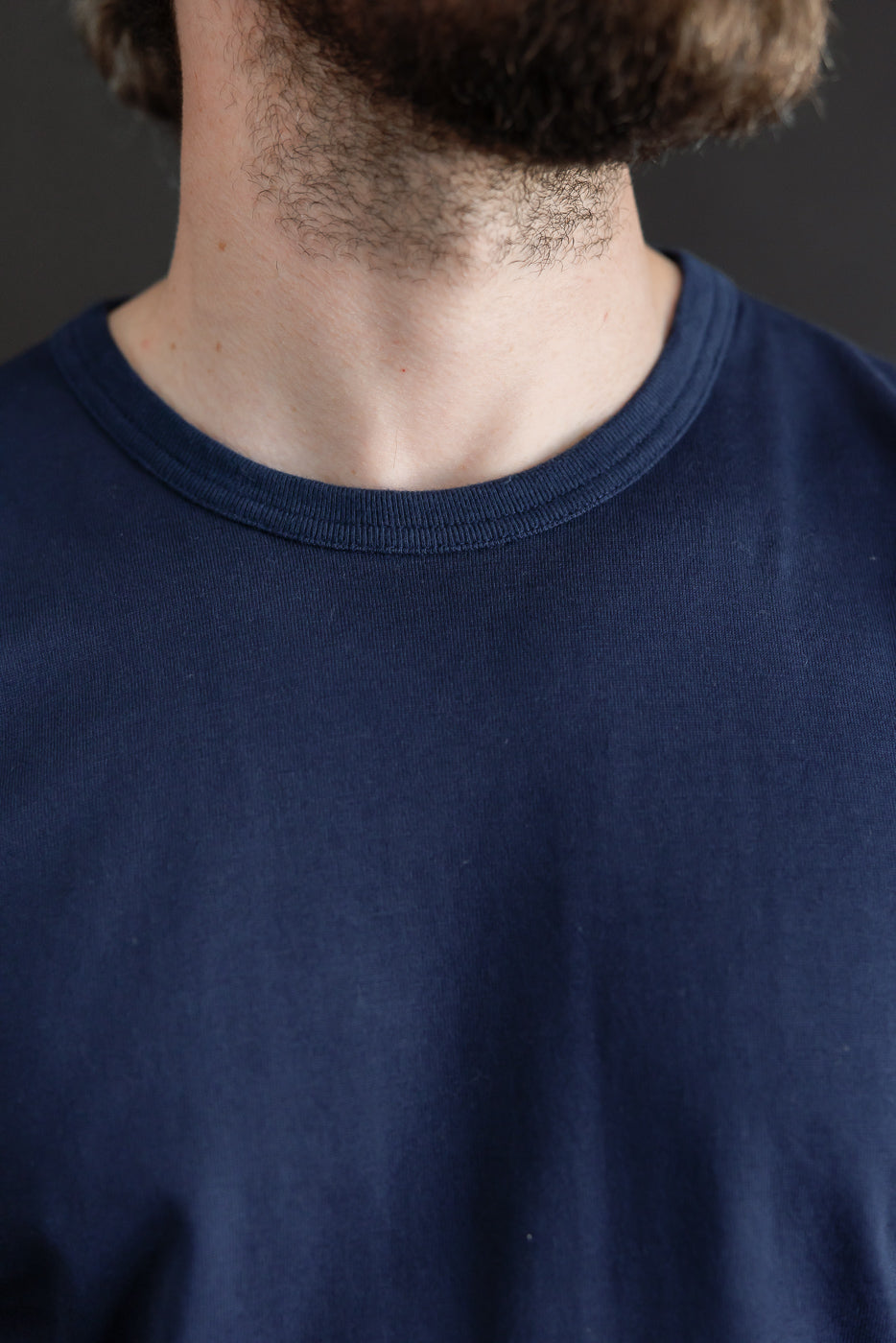 Close-up of the front neckline and collar of a navy blue crewneck t-shirt worn by a male model.