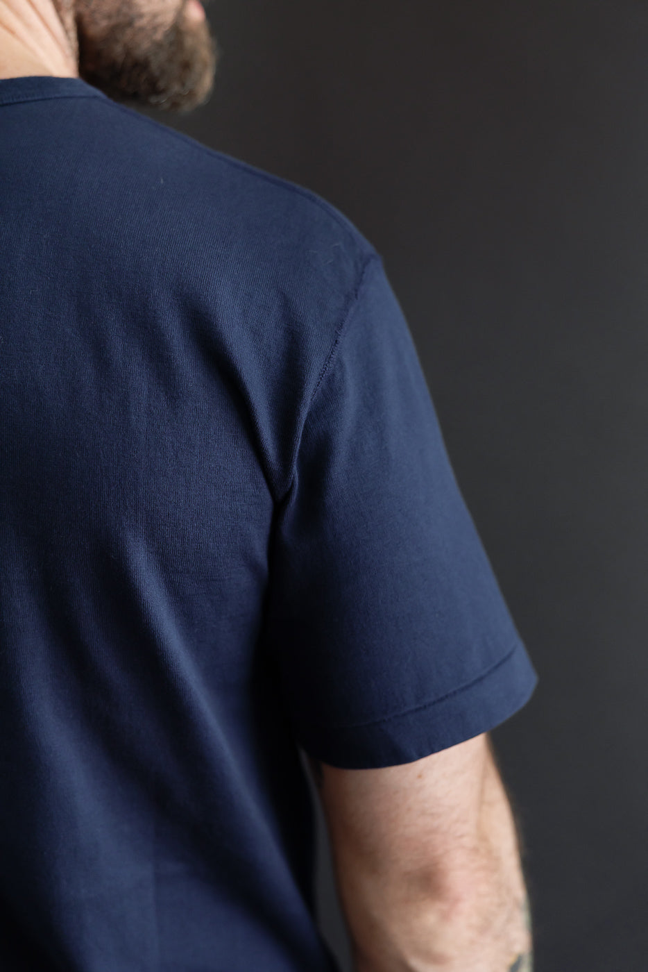Close-up back view of a male model wearing a navy blue crew neck t-shirt showing fabric texture.