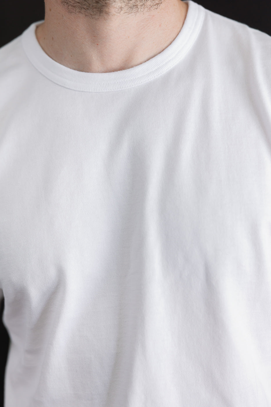 Close-up front view of a white crewneck t-shirt's ribbed collar and fabric texture on a male model.