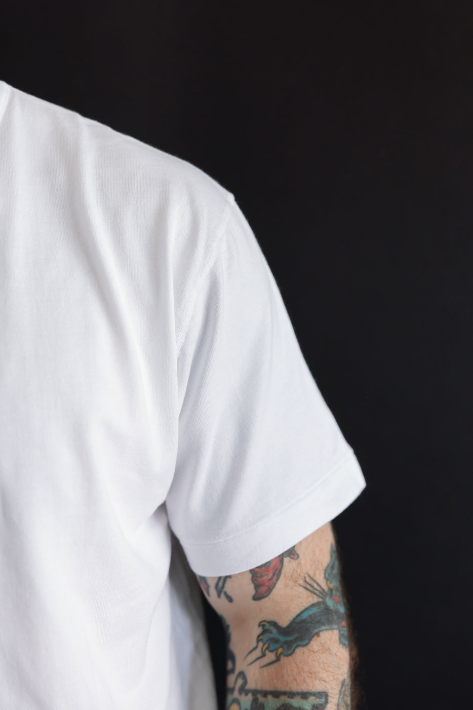 Close-up side view of a white cotton t-shirt sleeve on a male model with an athletic build.