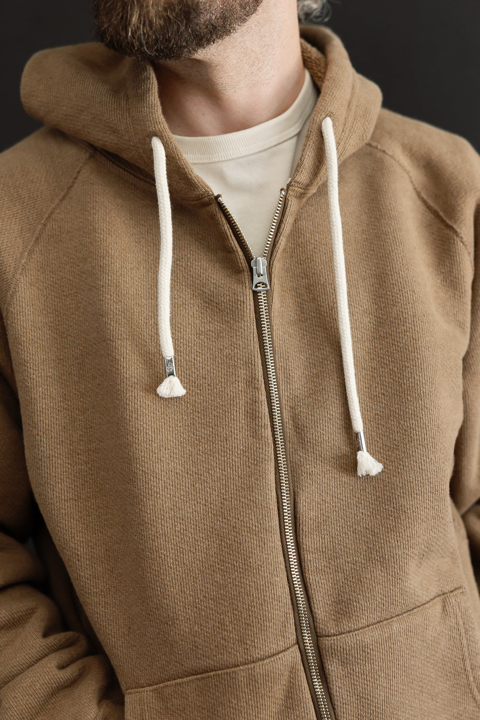 Close-up front view of a tan zip-up hoodie with white drawstrings on a male model.