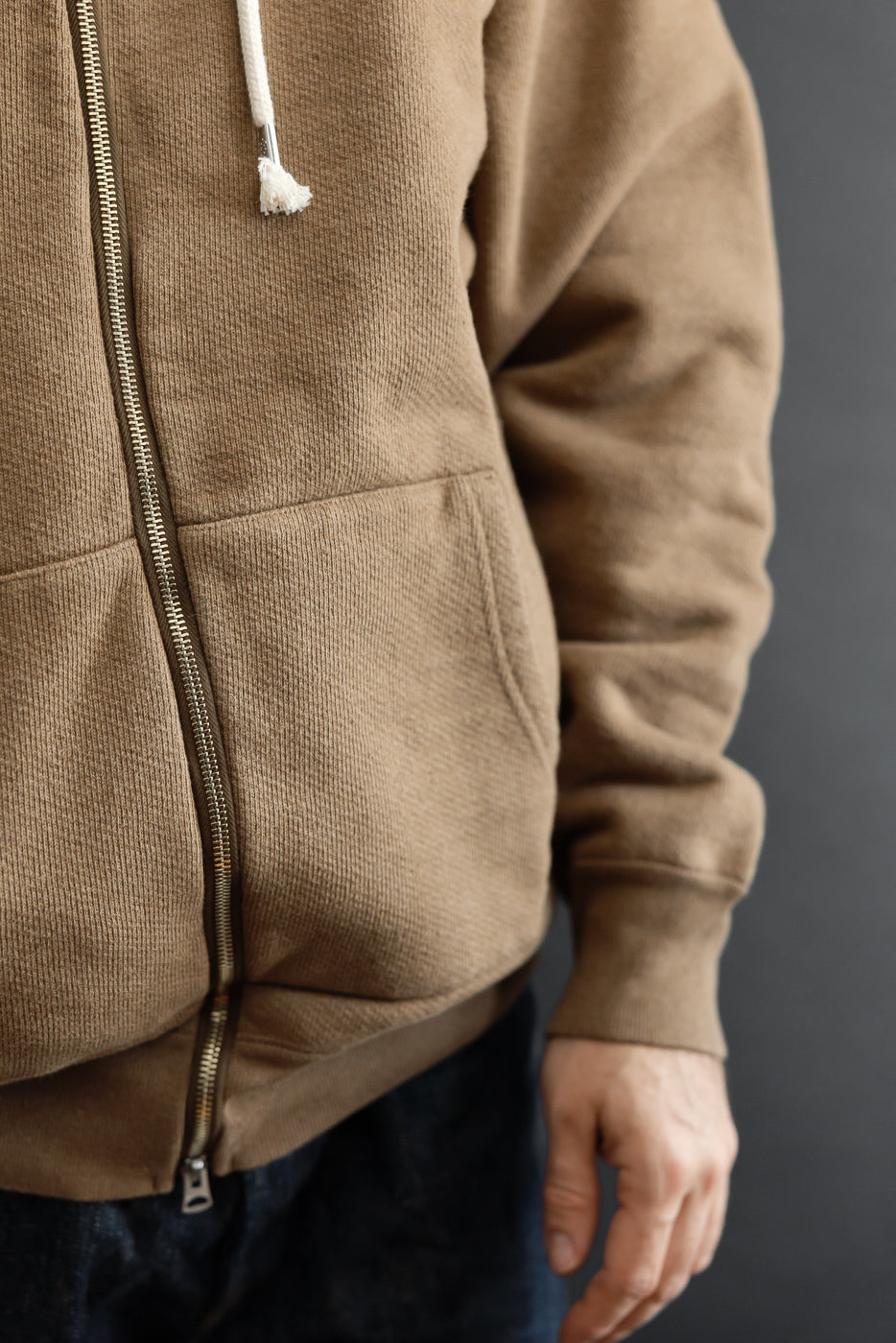Close-up of front right side of a tan zip-up hoodie on a male model, 5'9