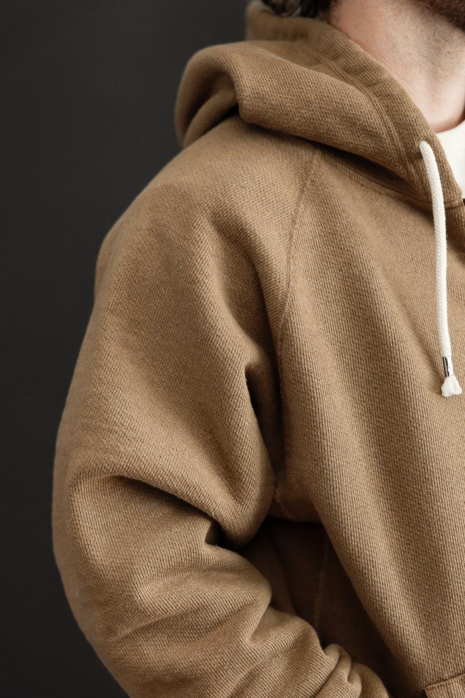 Close-up of the side and hood of a tan cotton hoodie worn by a male model.