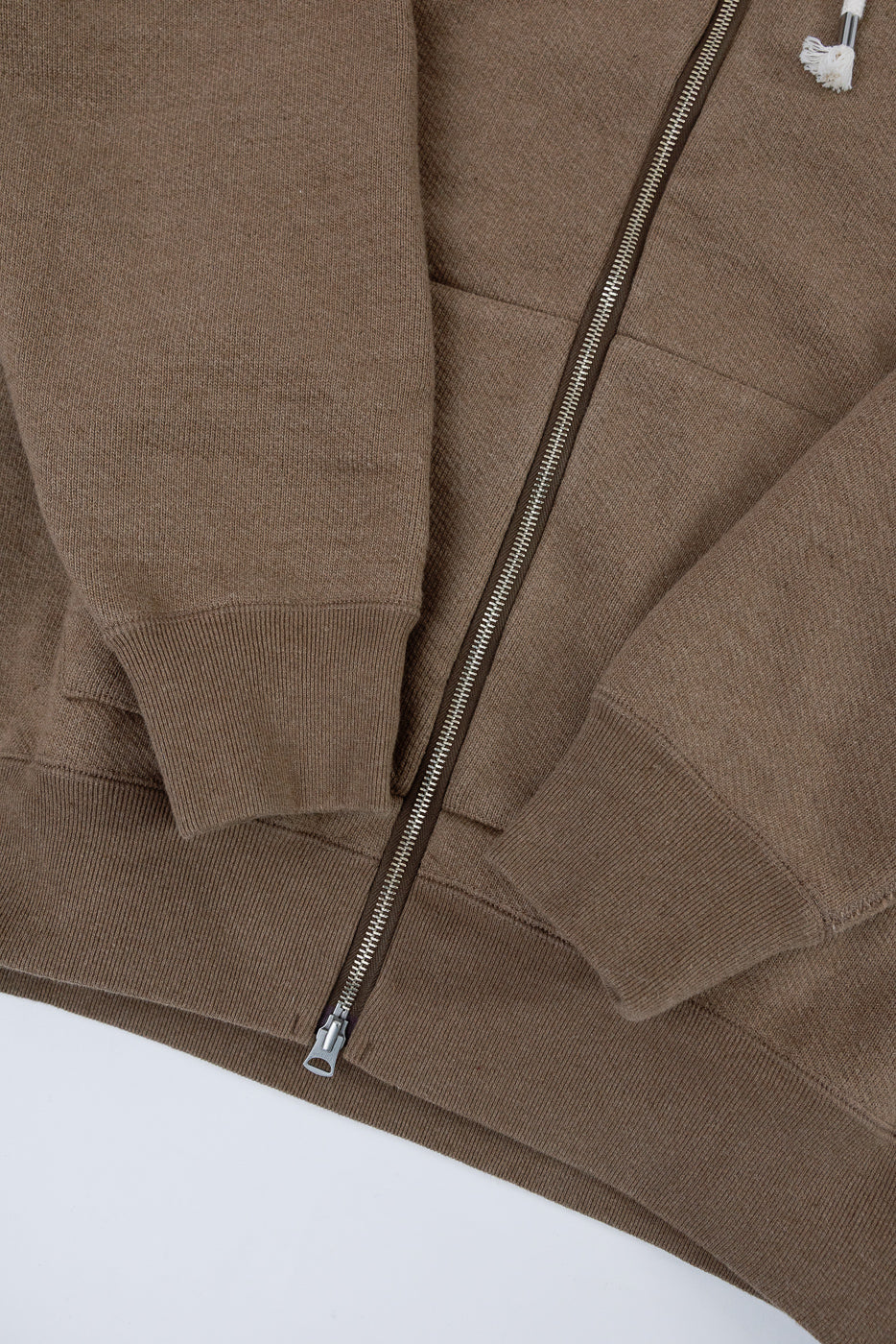 Close-up of the front of a brown zip-up hoodie showing fabric texture, zipper, and ribbed cuffs.