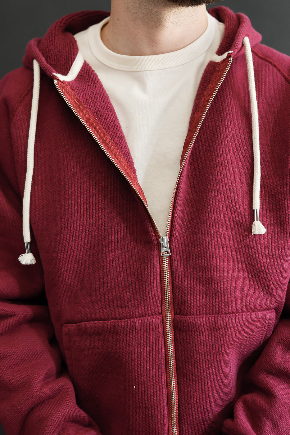Close-up front view of a burgundy zip-up hoodie with white drawstrings on a male model.