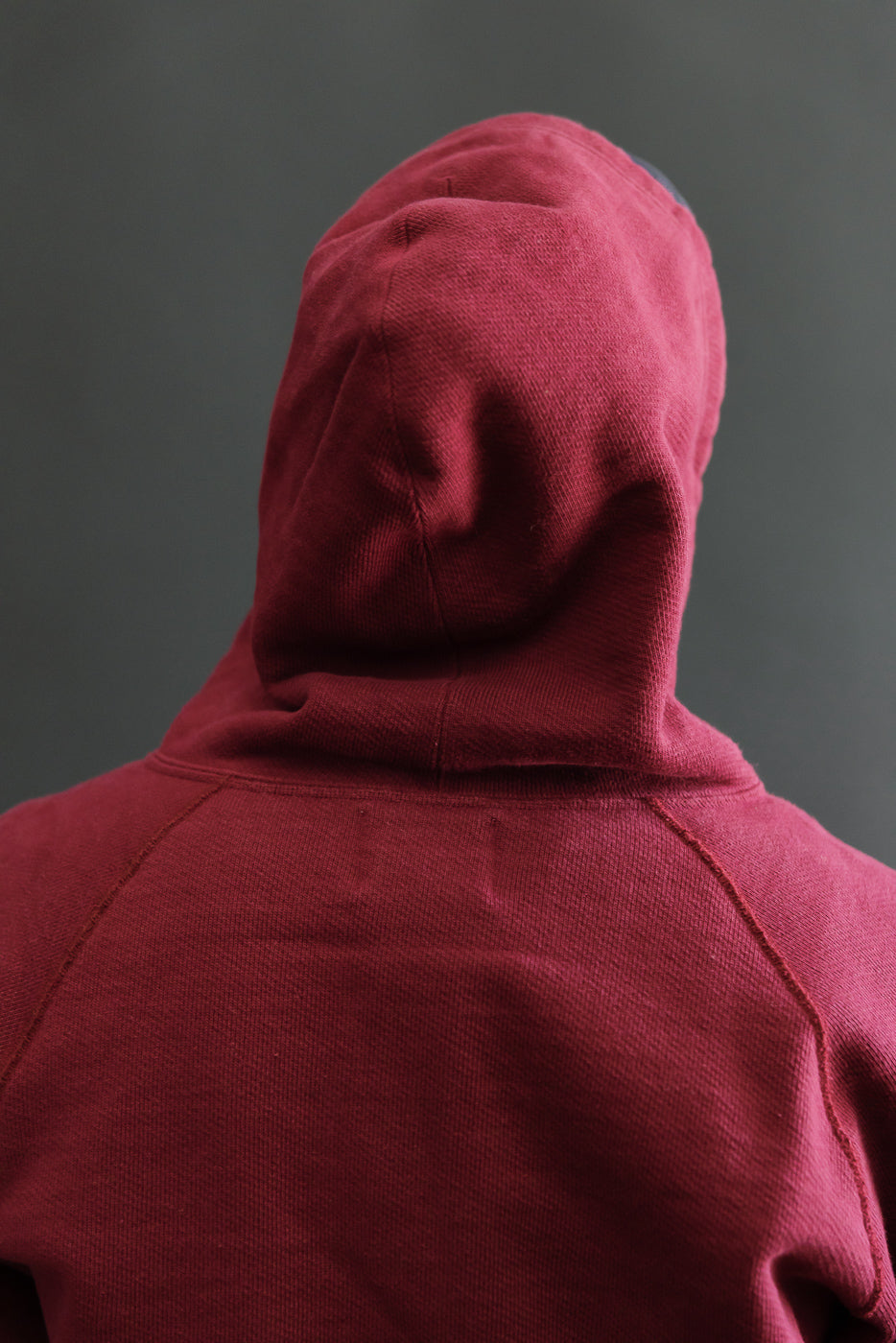 Back view close-up of a male model wearing a maroon hooded sweatshirt showing fabric texture.