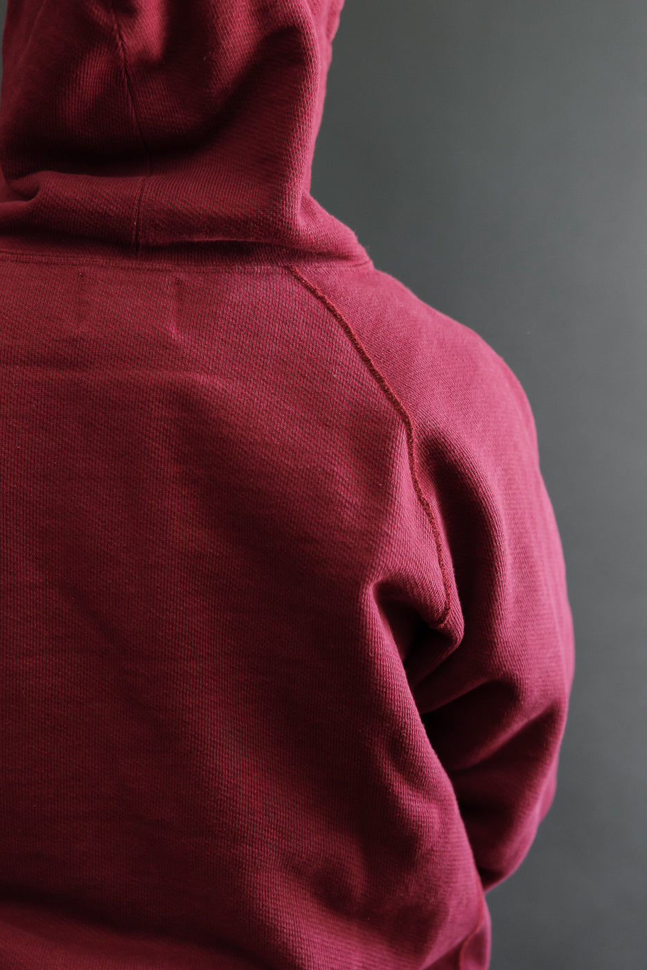 Close-up of the back and right side of a maroon textured hoodie fabric.