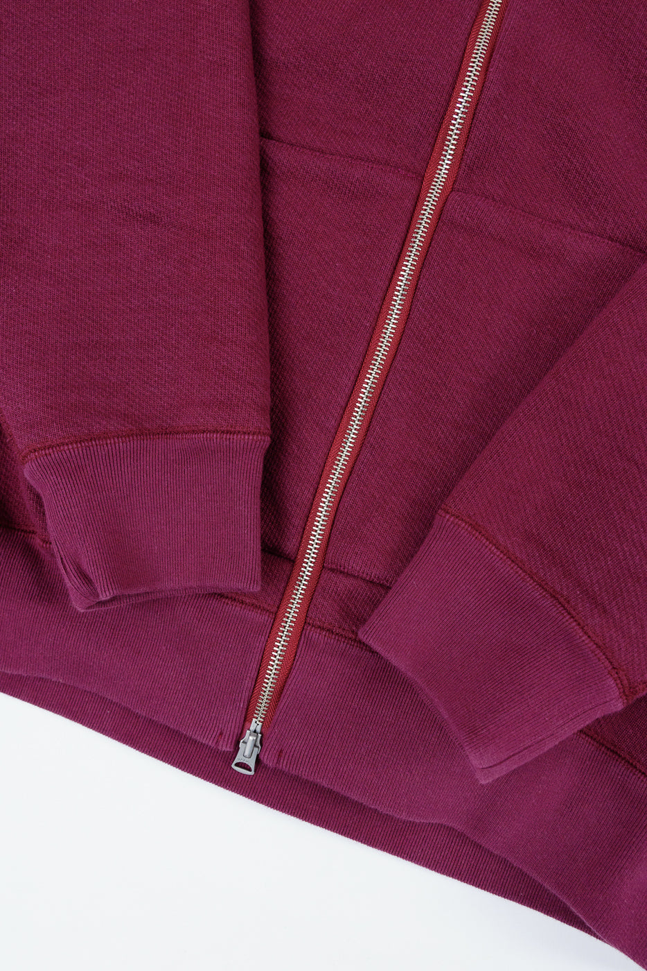 Close-up front view of a burgundy zip-up sweatshirt showing the silver metal zipper and fabric texture.
