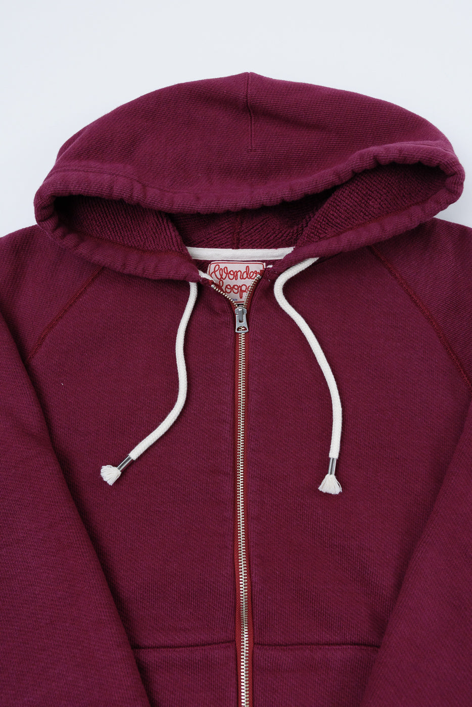 Close-up front view of a burgundy zip-up hoodie showing the hood, drawstrings, and zipper.