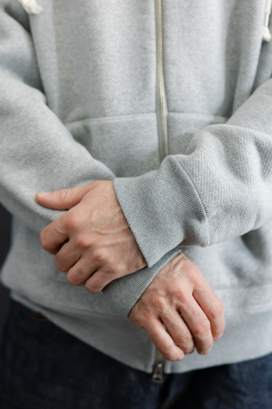 Close-up of the front sleeve and ribbed cuff of a light grey zip-up hoodie on a male model.