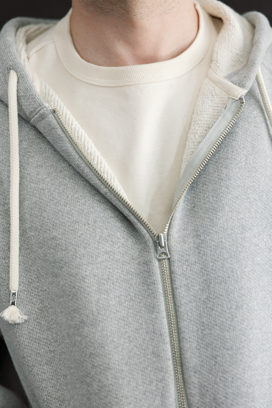 Close-up front view of a male model wearing a grey zip-up hoodie over a white t-shirt.