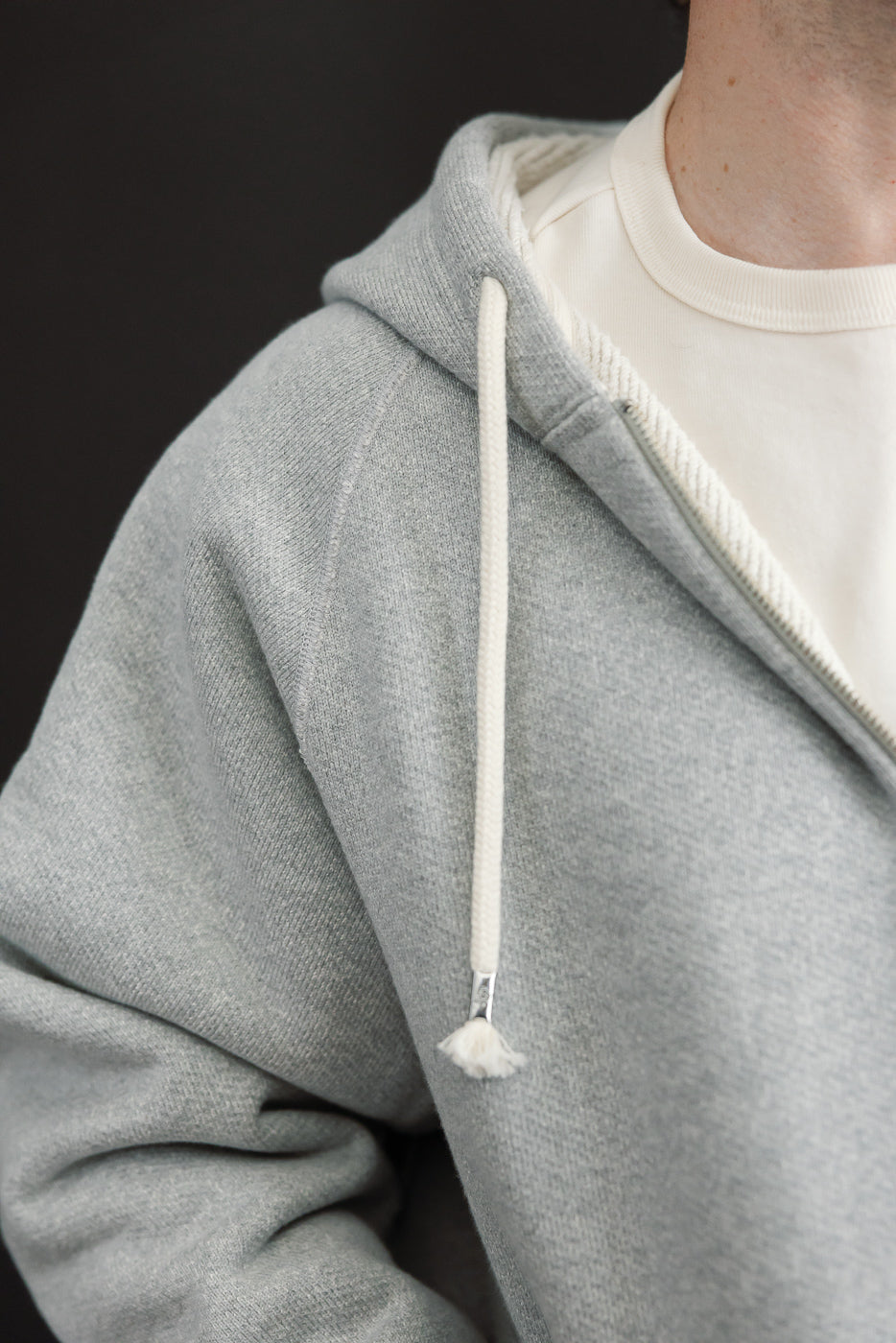 Close-up of the front left side of a male model's grey heathered cotton hoodie with white drawstring.