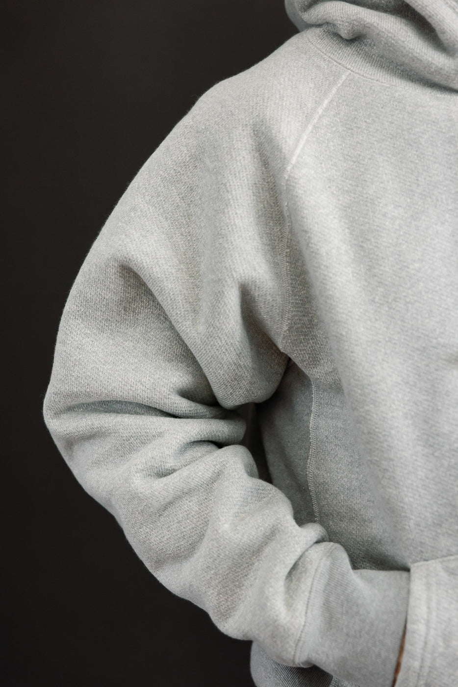 Close-up side view of a light grey hoodie's sleeve and shoulder on a male model, 5'9