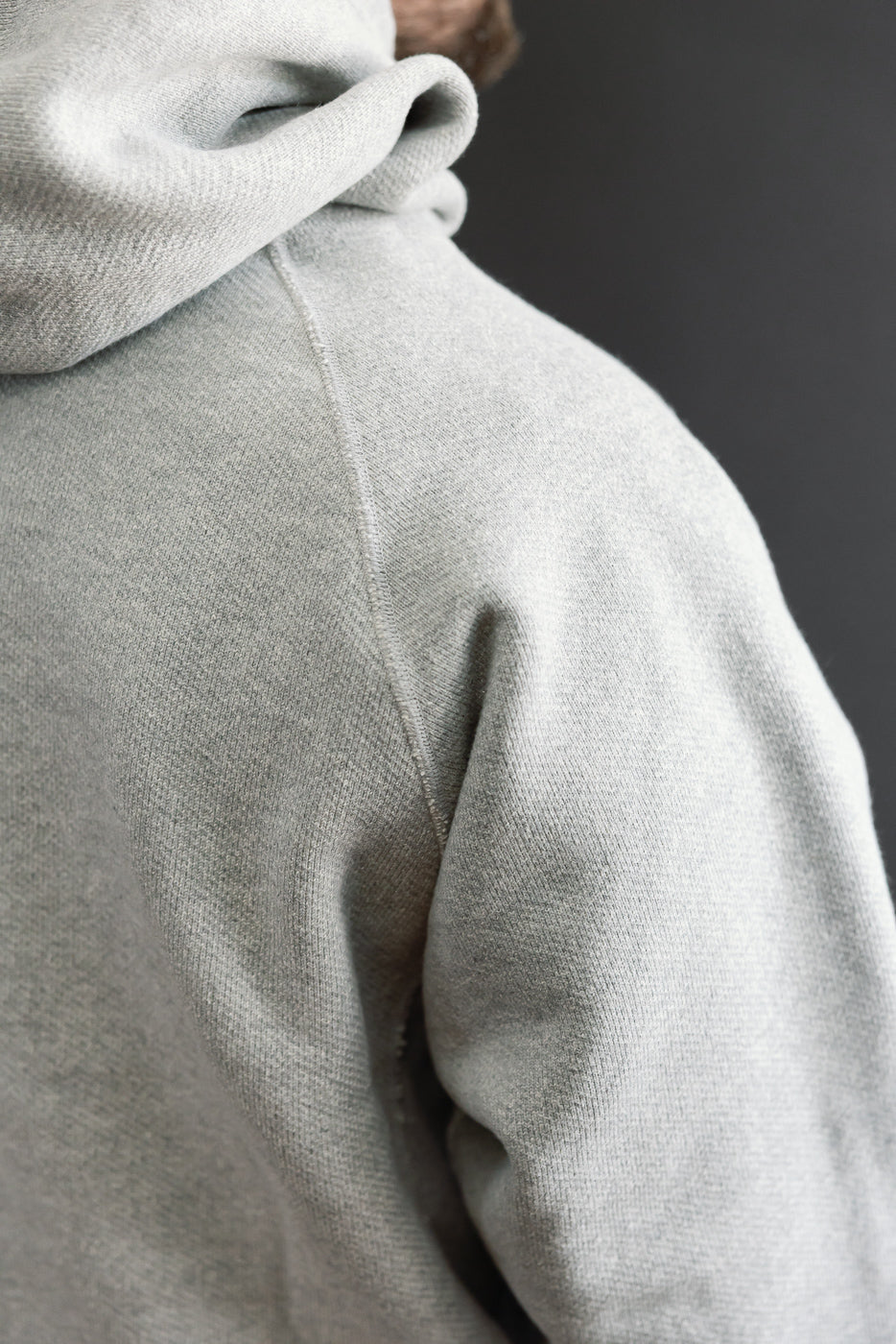 Close-up of the back shoulder and hood of a grey hoodie on a male model, 5'9