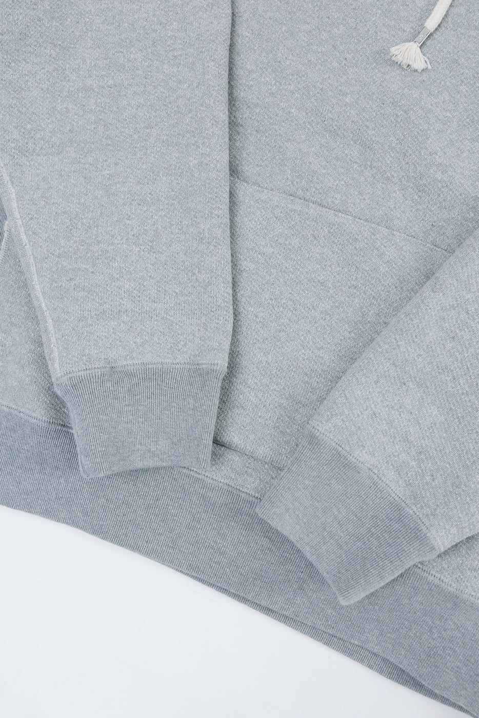 Close-up of the front of a grey hoodie showing the fabric texture, cuff, and bottom hem.