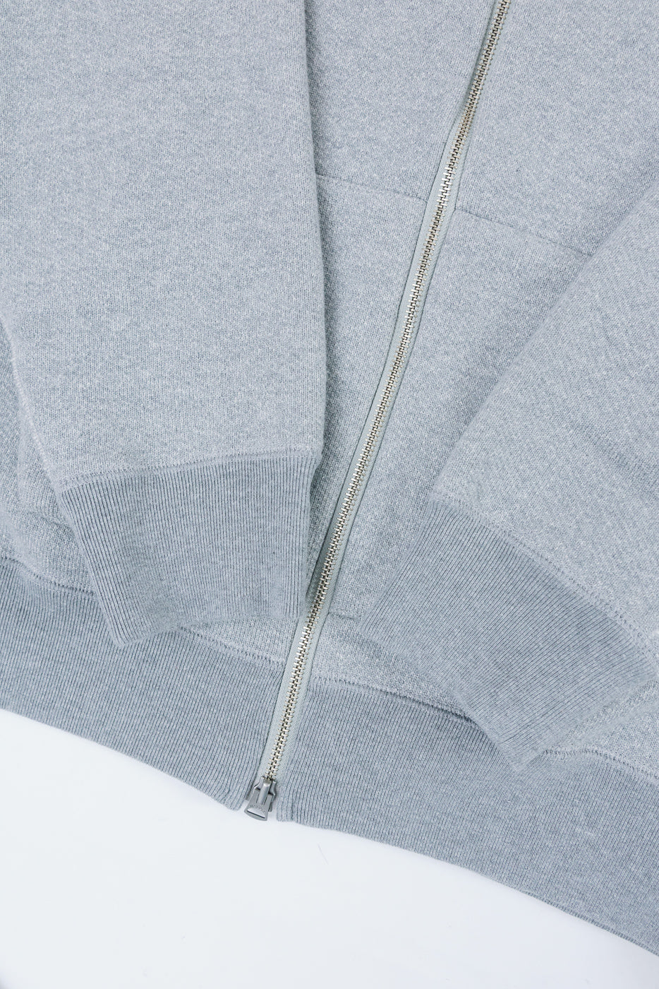 Close-up front view of a grey zip-up sweatshirt showing the metal zipper and ribbed cuff detail.