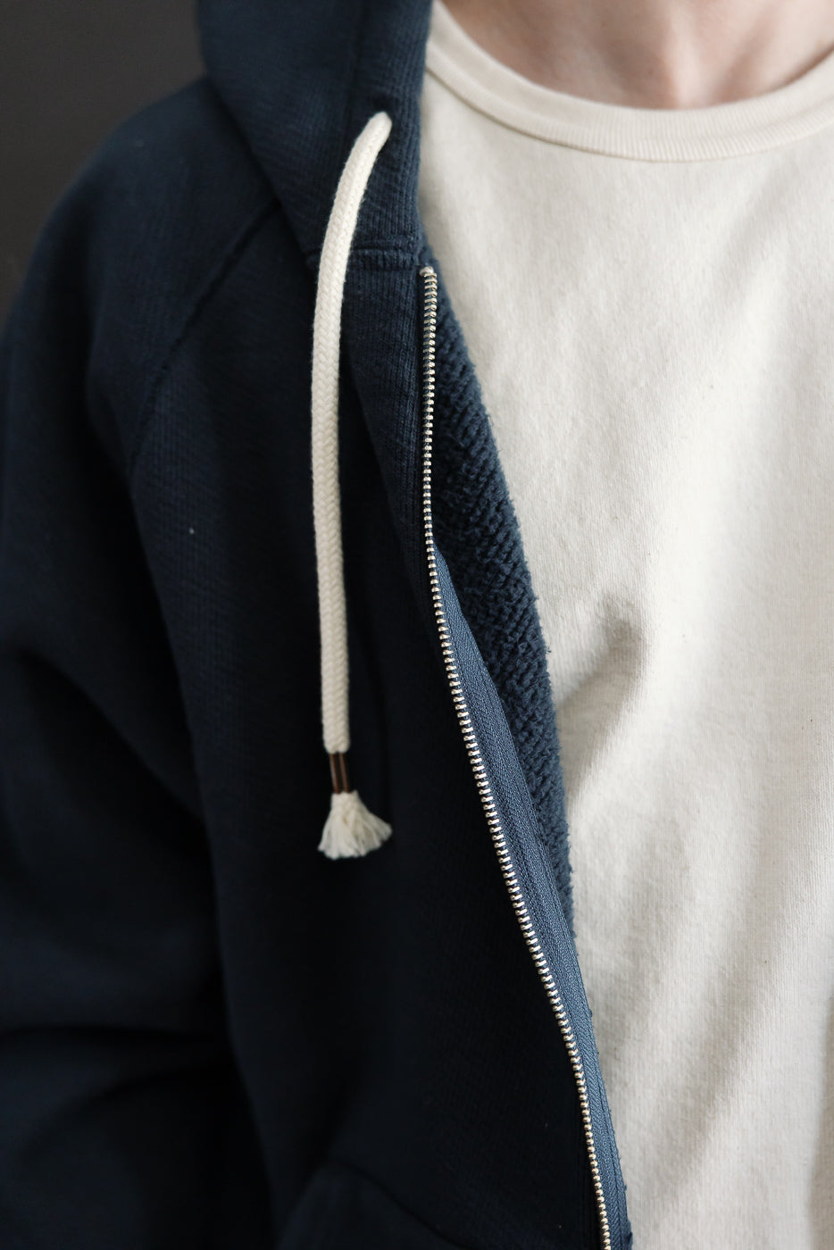 Close-up of the front left side of a navy blue zip-up hoodie, showing the zipper and white drawstring.