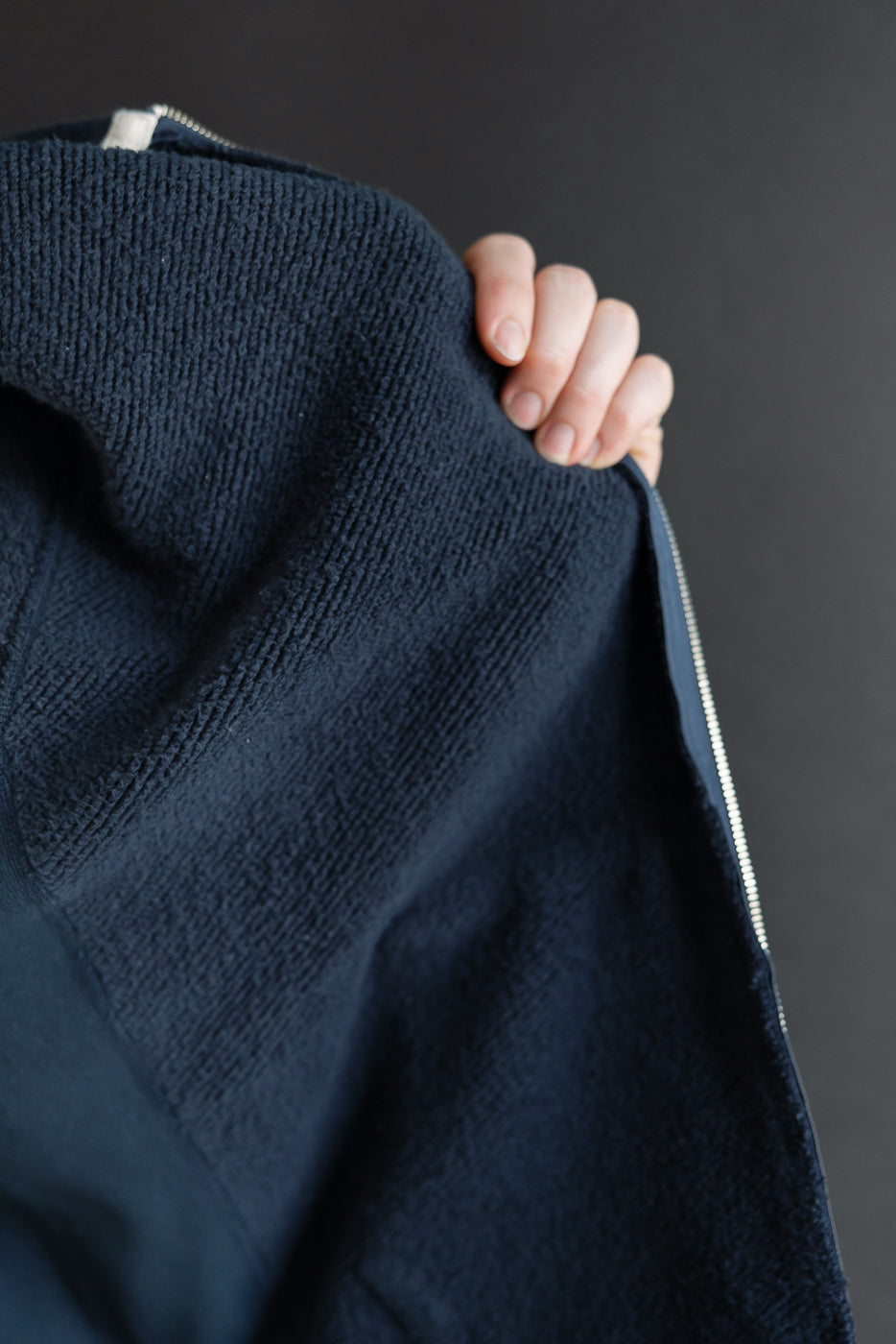 Close-up of the navy blue textured terry cloth fabric and zipper detail on a garment.