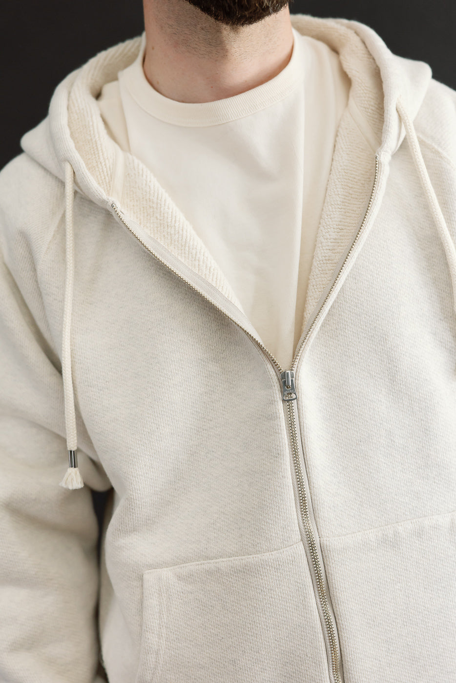Close-up front view of a cream zip-up hoodie with textured fabric and silver zipper detail.