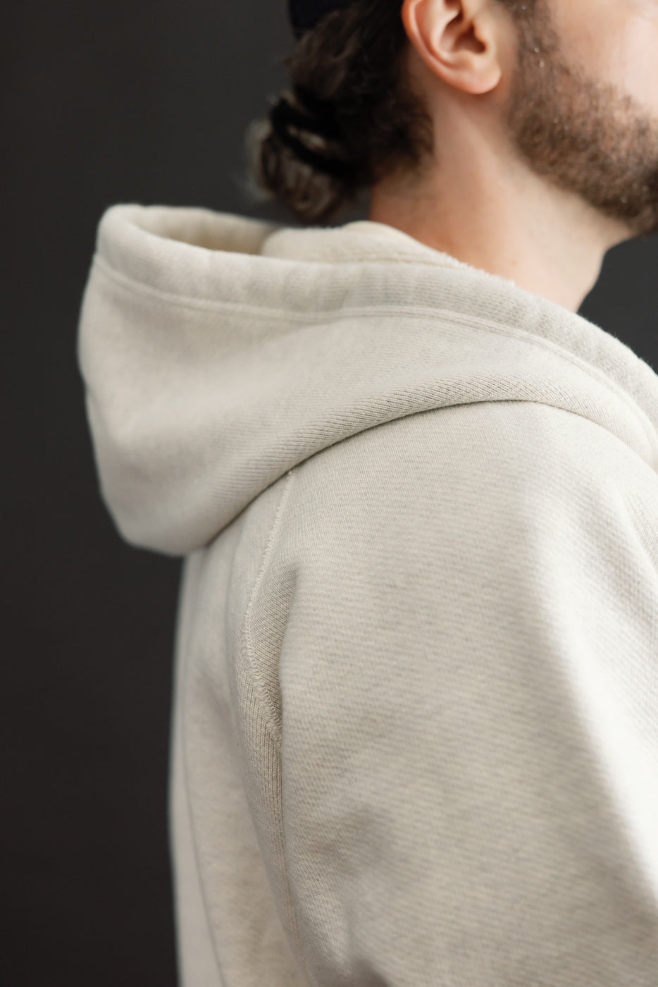 Close-up side view of a cream hoodie's hood and shoulder texture on a male model.