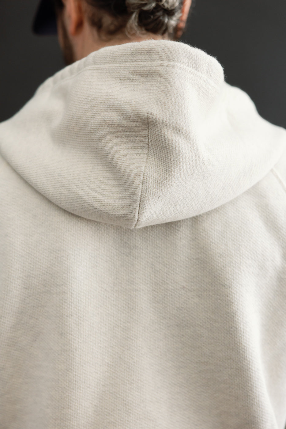 Close-up back view of a cream hooded sweatshirt showing the fabric texture and hood detail.