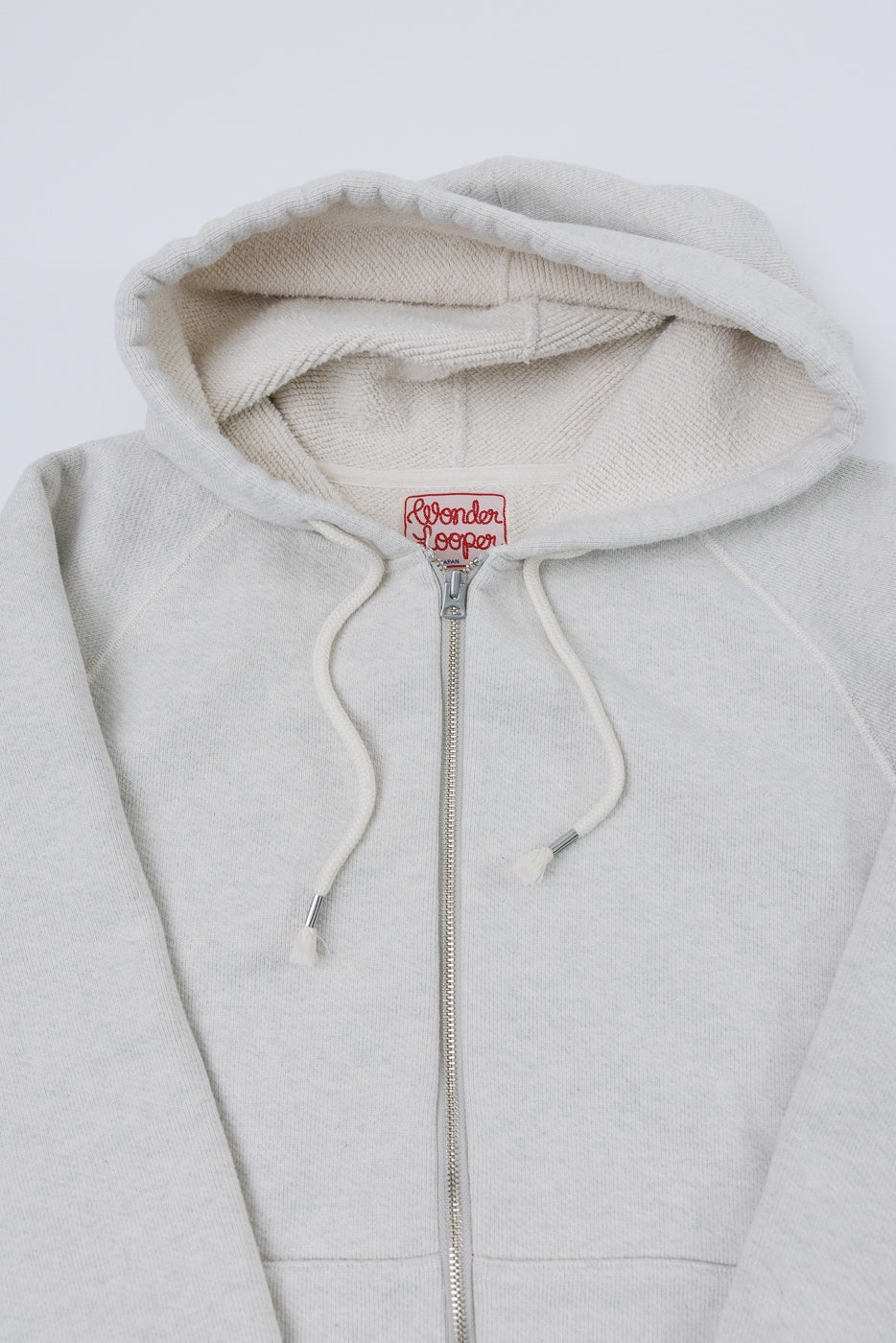Flat lay front view close-up of a cream zip-up hoodie showing the hood, zipper, and drawstrings.