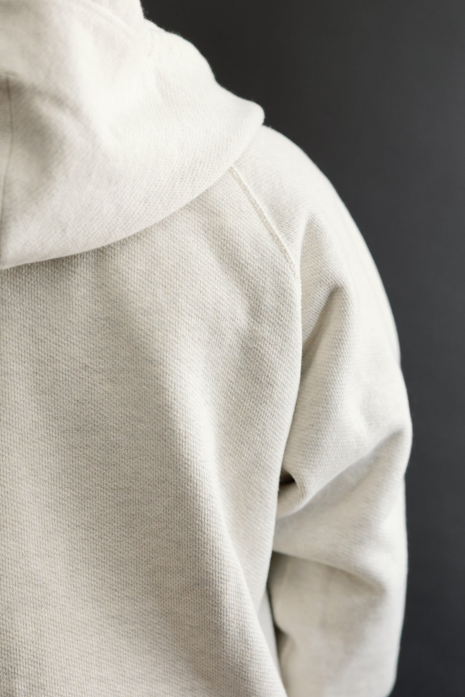 Close-up back view of a cream hoodie showing the fabric texture and hood detail.