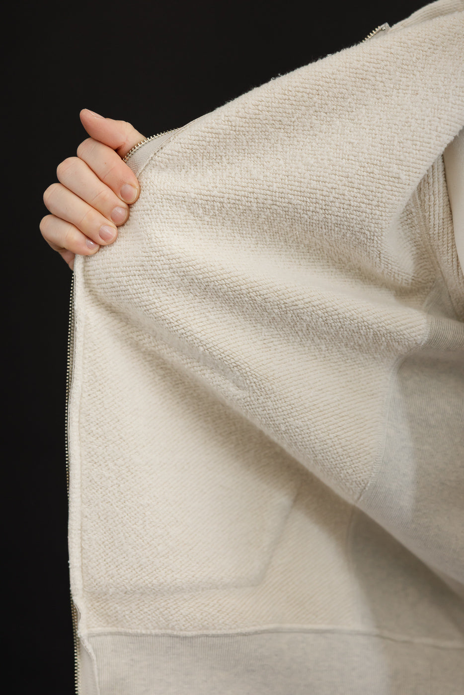 Close-up of the interior side view of a cream textured fleece zip-up hoodie.