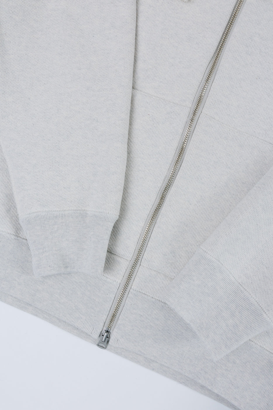 Close-up front view of a light grey zip-up hoodie showing the silver zipper and fabric texture.