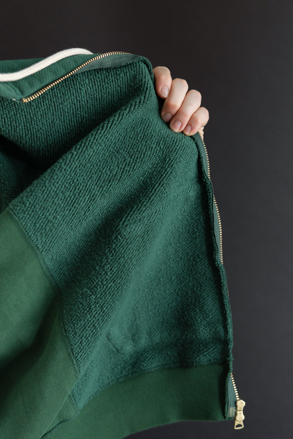 Close-up of the interior terry cloth fabric texture and gold zipper on a green garment.