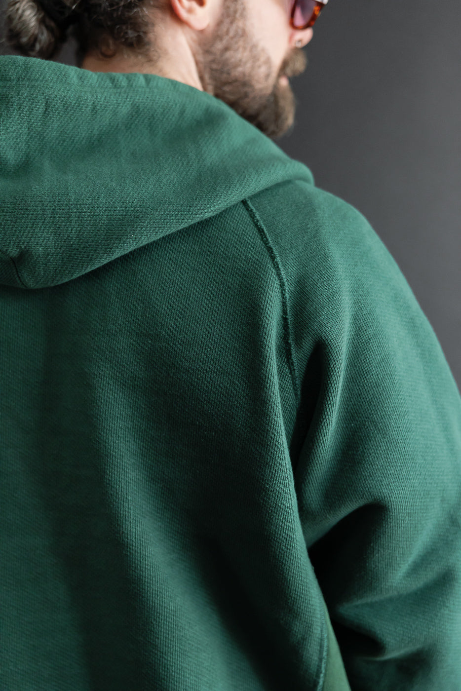 Close-up back view of a green hooded sweatshirt showing heavy fleece fabric texture.
