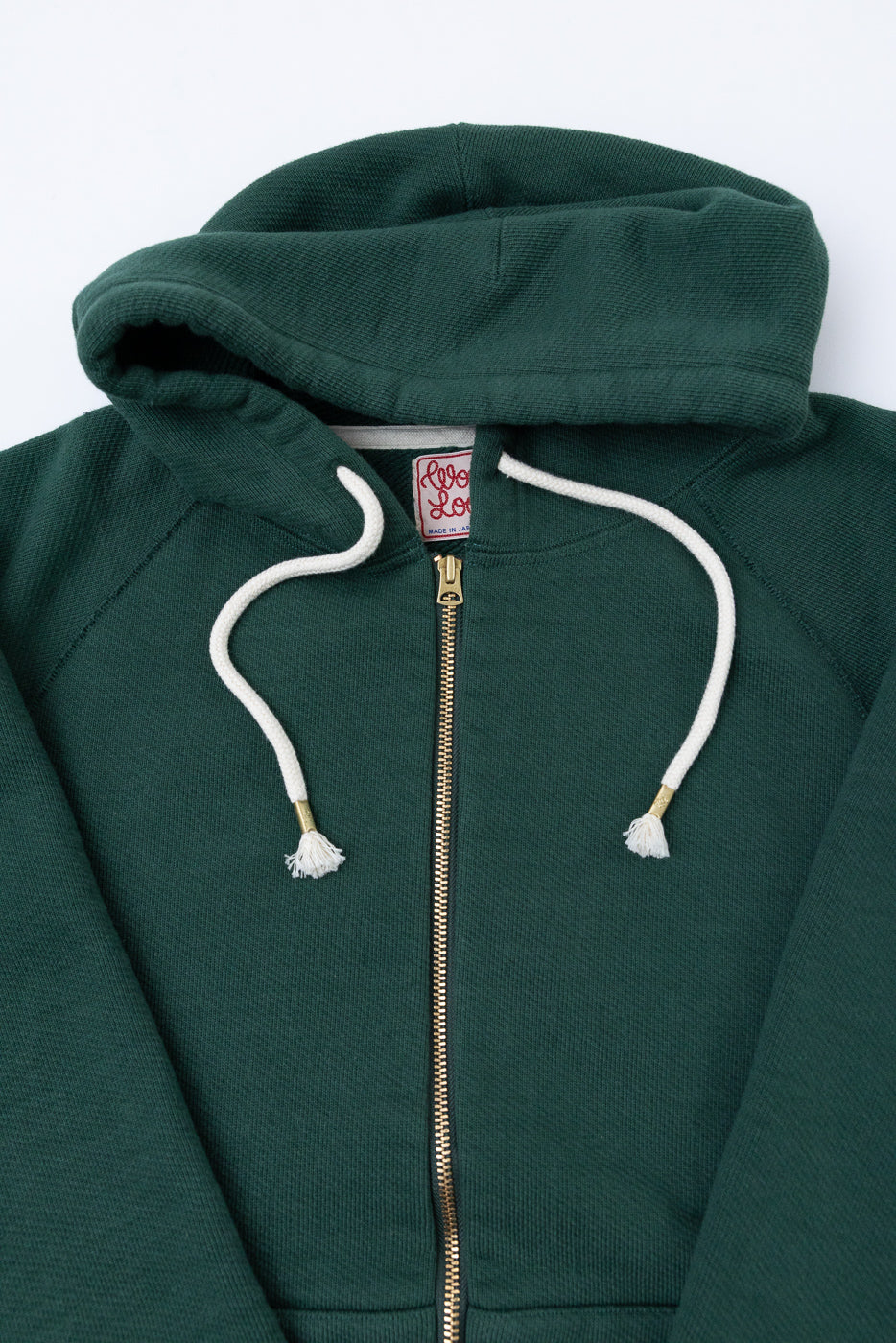 Close-up front view of a dark green zip-up hoodie showing the zipper, hood, and white drawstrings.