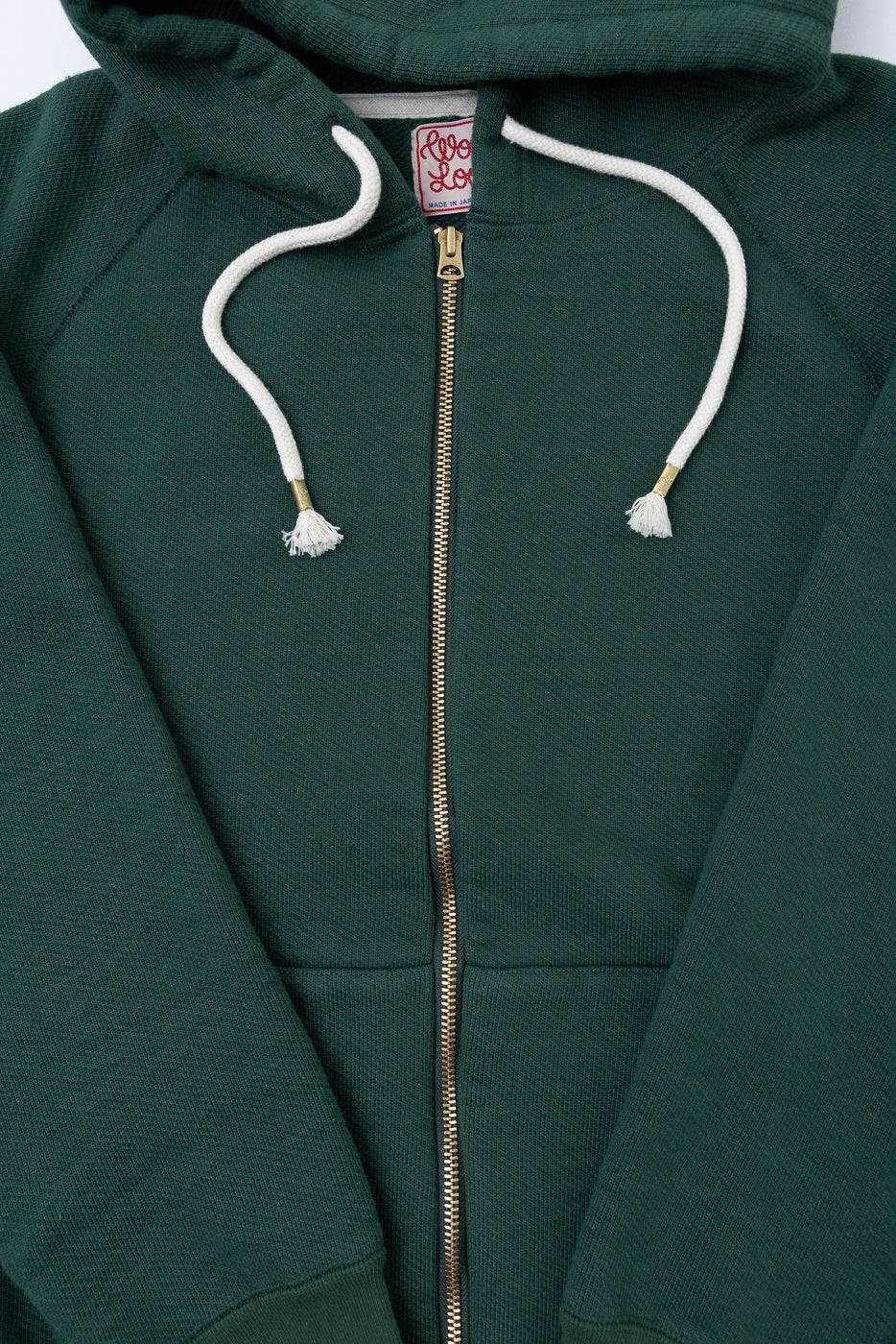 Close-up front view of a dark green zip-up hoodie showing the brass zipper and white drawstrings.