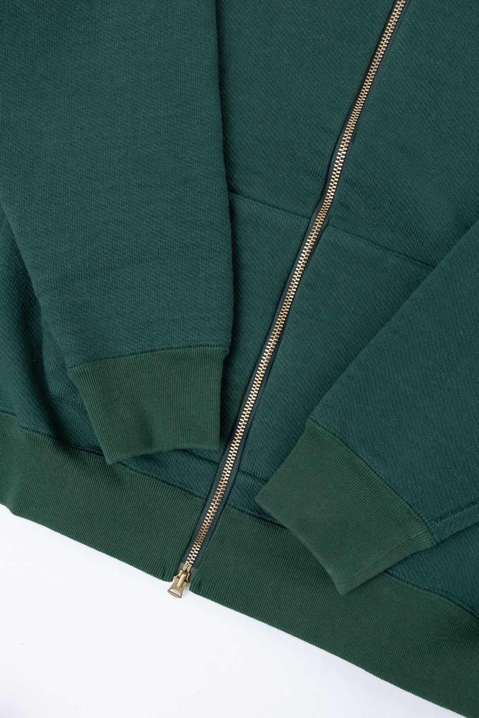 Close-up front view of a green zip-up hoodie showing the metal zipper and ribbed cuffs.