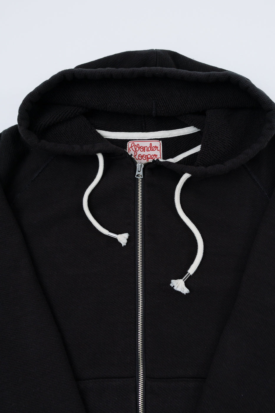 Close-up of the front neck and zipper area of a black hoodie featuring a red Wonder Looper tag.