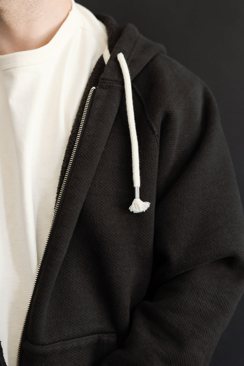 Close-up of the front left side of a male model wearing a black hooded sweatshirt over a white t-shirt.