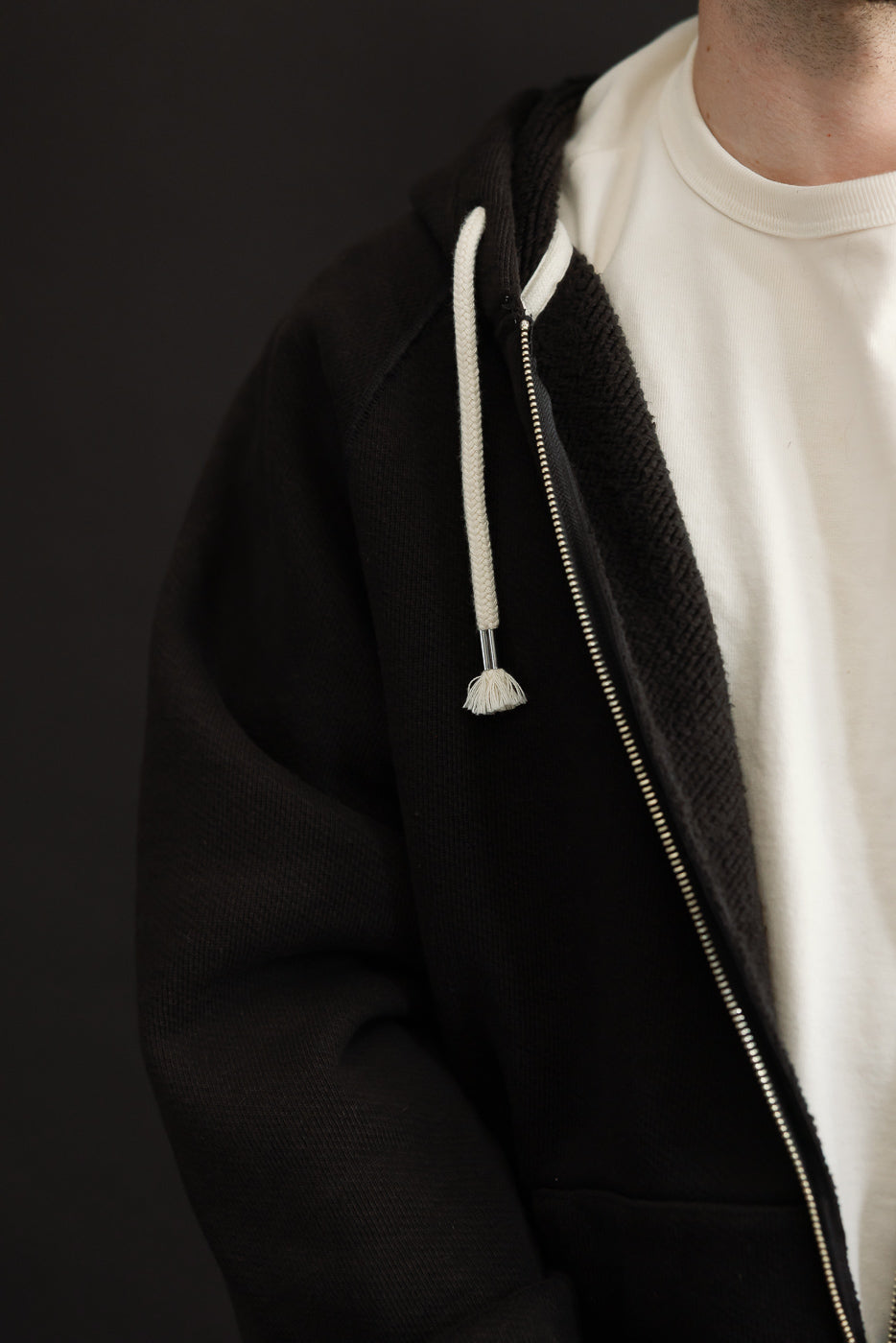 Side view close-up of a black zip-up hoodie with white drawstrings on a male model.